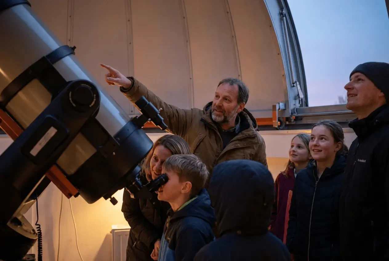 Visitors at an observatory looking through a large telescope into the starry night sky during a public tour